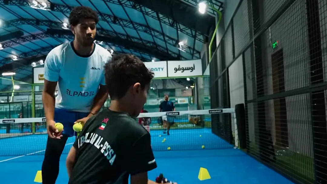 A coach feeding balls to a young player during a drill